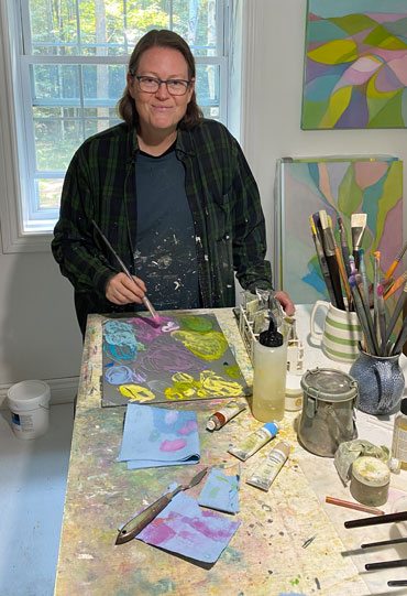 Lindsay mixing paint in her art studio wearing a paint splattered shirt