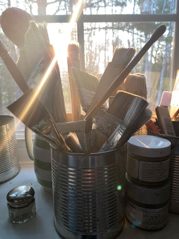 sunlight streaming through a window filled with brushes, tins and jars